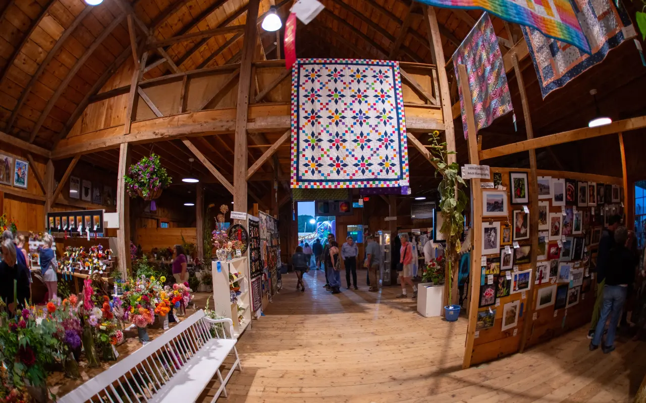 Quilts hanging from the timber beams inside the Agricultural Hall during the fair with exhibits below