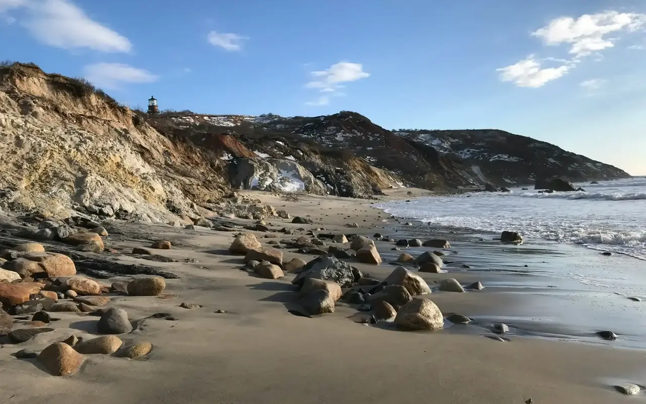 Boulders on the sand at Moshup Beach with the Gay Head cliffs rising above and the lighthouse on top