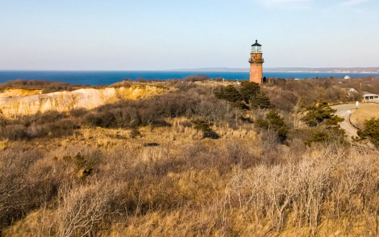 Red brick lighthouse standing above golden moorland in Aquinnah