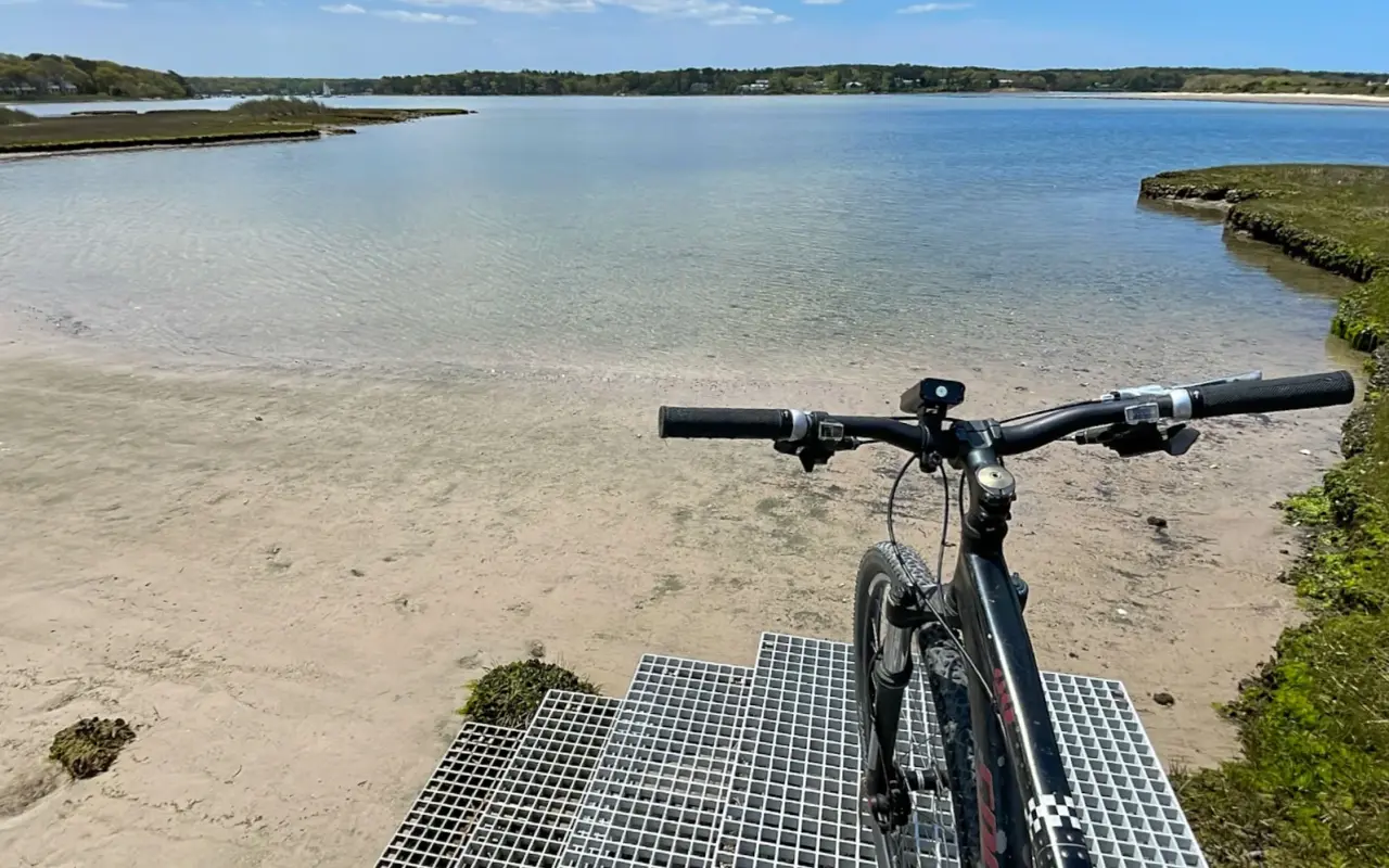 Bicycle handlebars overlooking a calm tidal pond and sandy shoreline