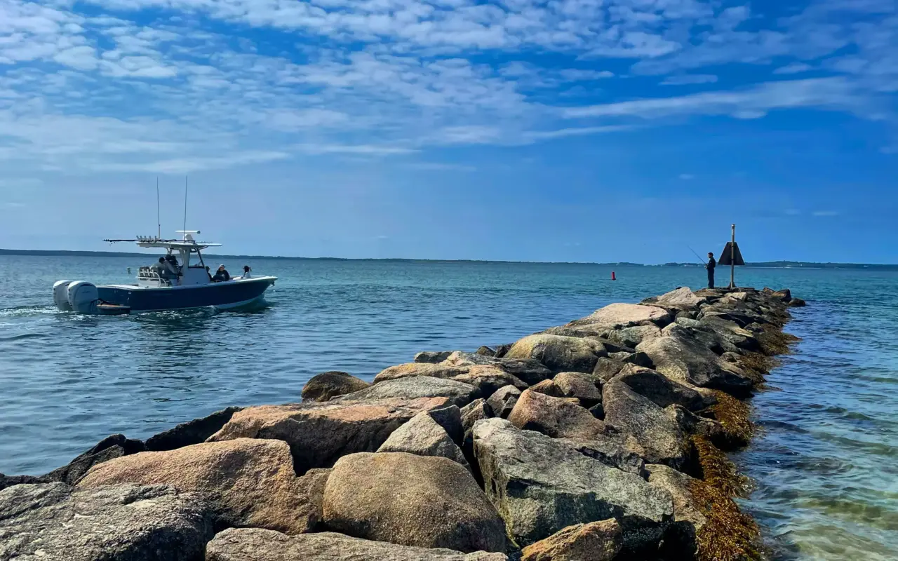 A boat running past the stone jetty at Vineyard Haven with an angler at the end