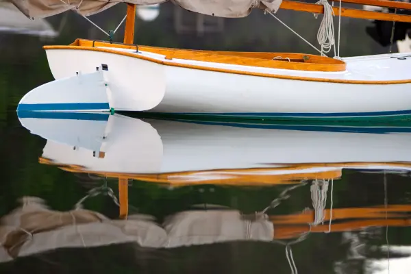 Wooden sailboat bow reflected in calm harbor water