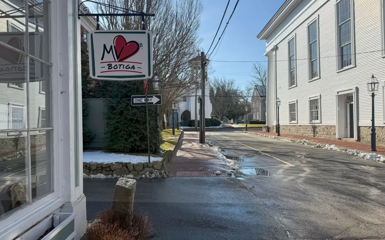 A shop sign on Church Street in Edgartown with white clapboard buildings and a wet street on a winter day