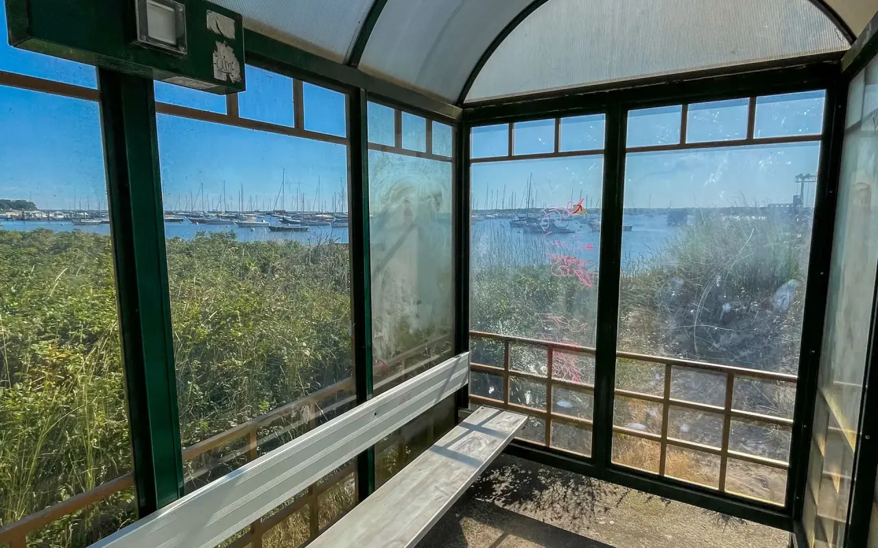 Glass bus shelter in Vineyard Haven with the harbor visible behind it on a sunny day
