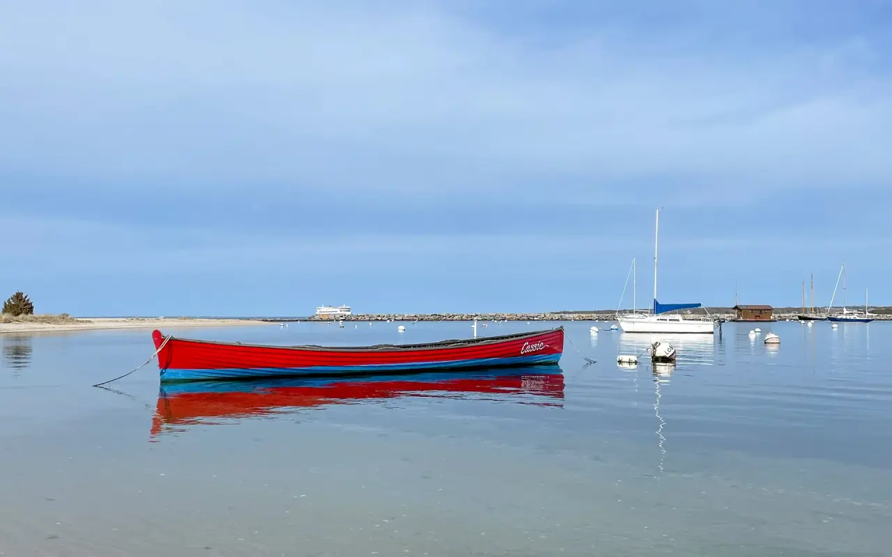 A red rowboat floating on calm water in Vineyard Haven harbor