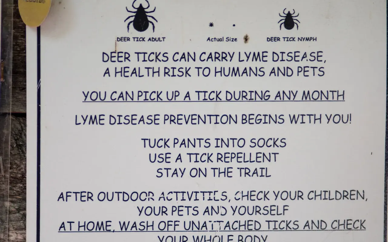 Trailhead sign warning that deer ticks carry Lyme disease with prevention tips