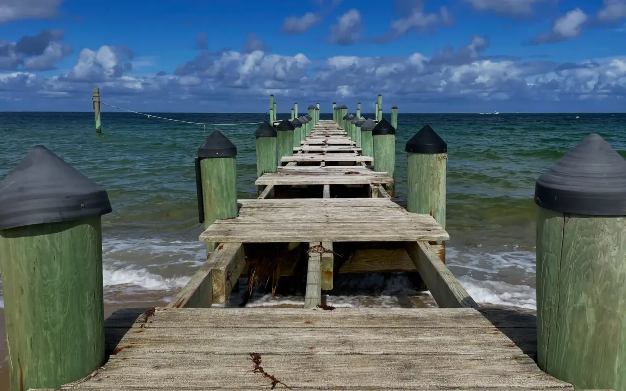 Wooden pier on Chappaquiddick with planks removed for winter, green capped pilings and choppy water beyond