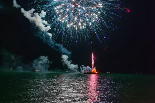 Fireworks exploding over the water with boats watching below