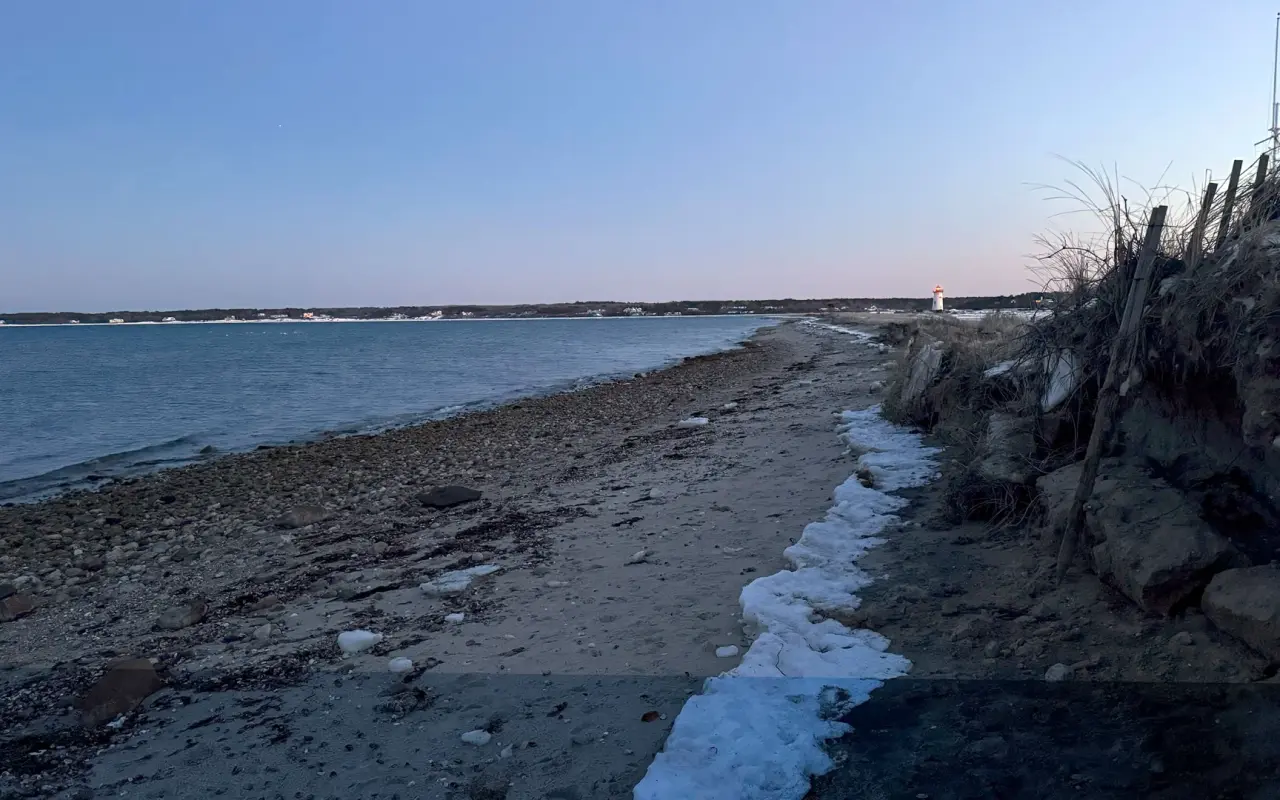 An empty pebbly beach in Edgartown at dusk with a line of foam along the tide and a lighthouse in the distance