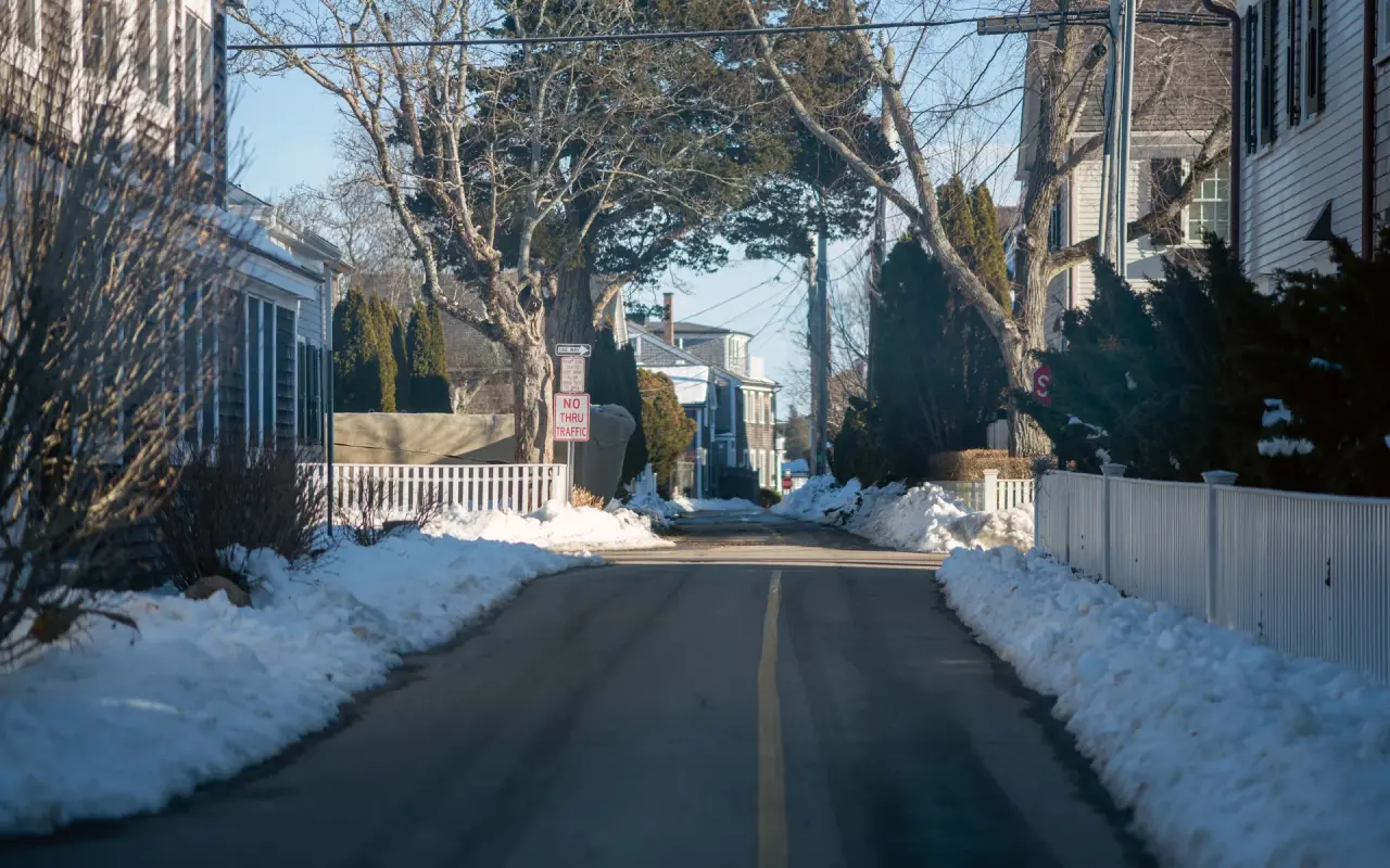 A residential street in Edgartown with snowbanks along white picket fences and shingled houses after a snowstorm
