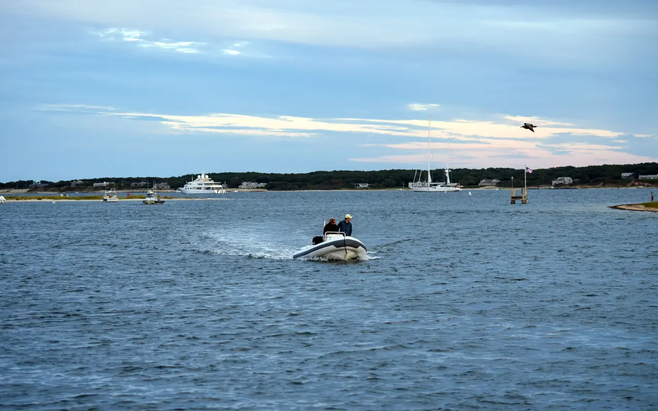 Small motorboat leaving Edgartown harbor with moored yachts and the far shore behind
