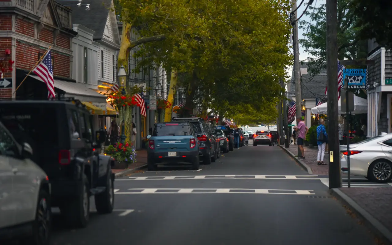 Main Street in Edgartown lined with parked cars, trees and American flags on a bright afternoon