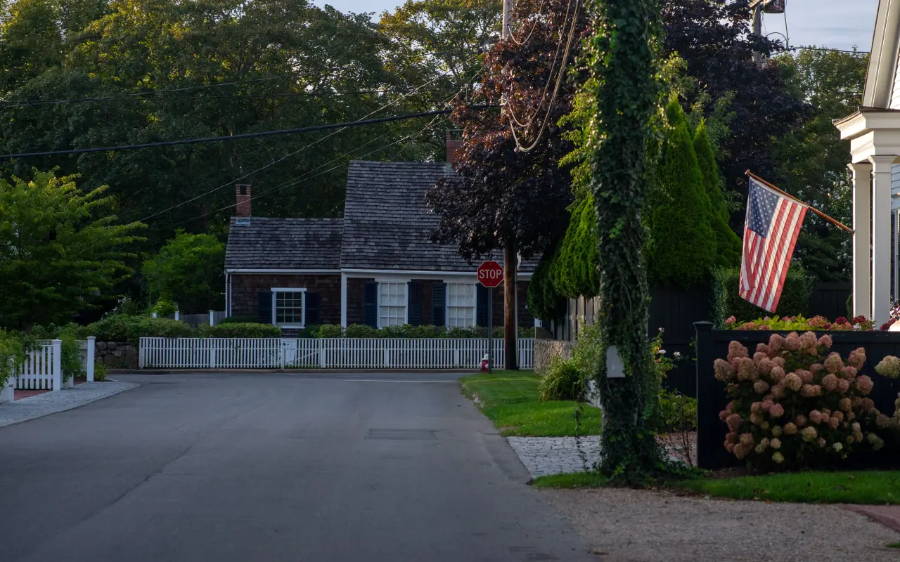 Gray shingled cottage with a white picket fence, blue hydrangeas and an American flag on a sunny Edgartown street
