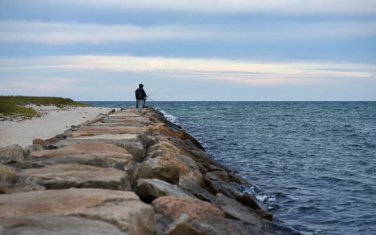 A lone angler standing at the end of a stone jetty in Oak Bluffs