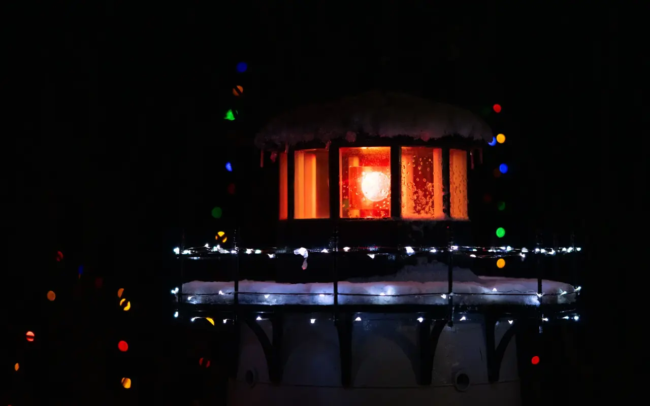 Lighthouse lantern room glowing warmly behind holiday string lights at night on Martha's Vineyard