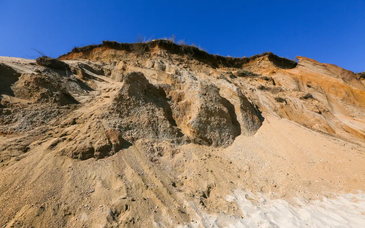 Eroded tan and gray clay bluffs above the sand at Lucy Vincent Beach in Chilmark under a deep blue sky