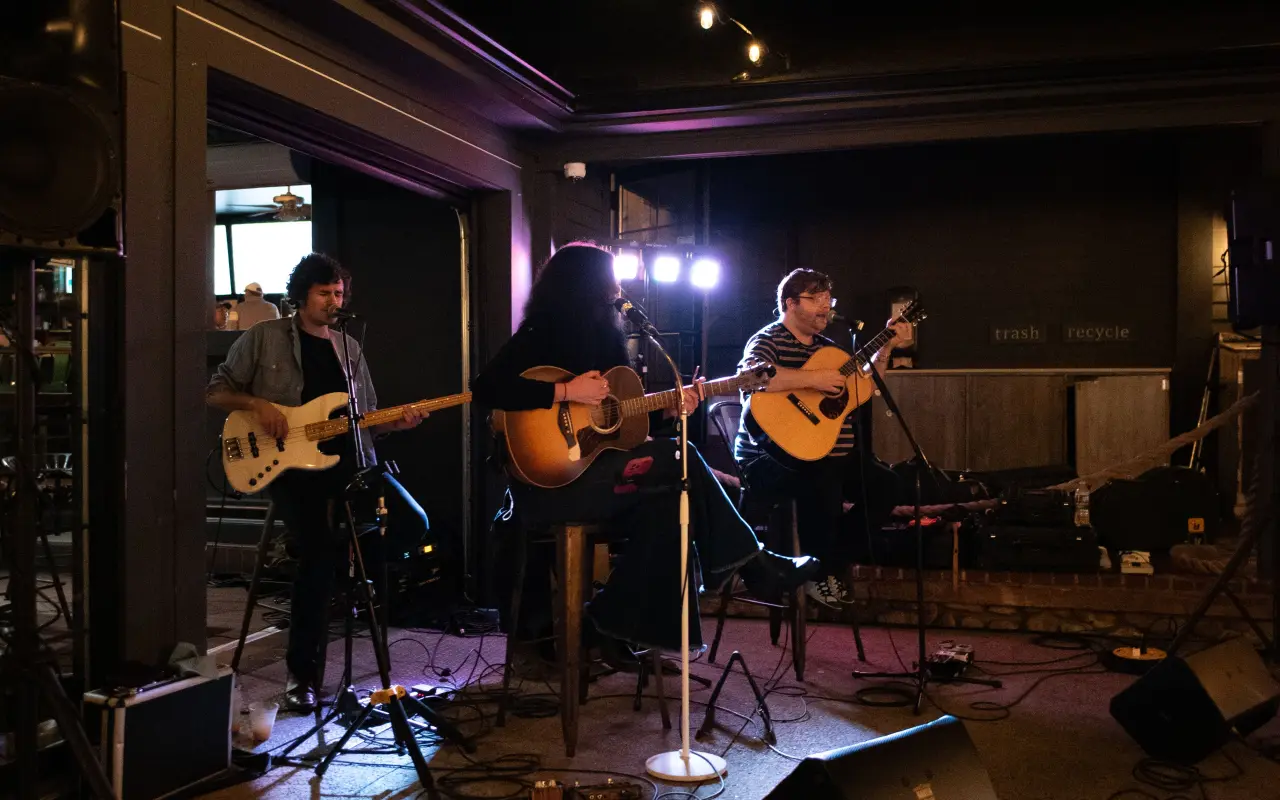A band with guitars and a bass playing on a dimly lit stage with stage lights behind them