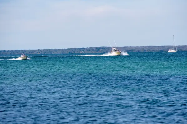Motorboats and a sailboat crossing blue water on a summer day