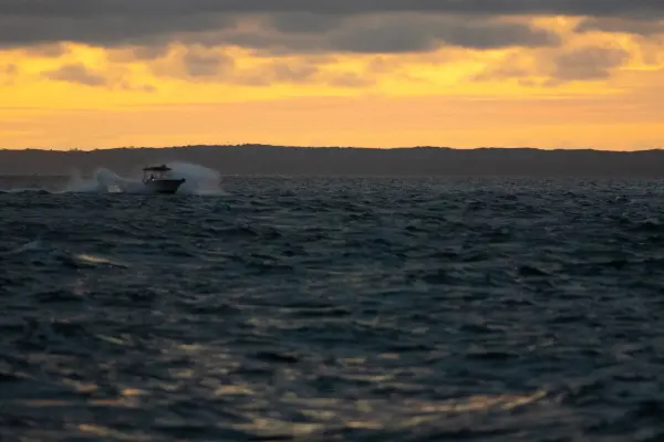 Powerboat crossing choppy water under a golden sunset sky
