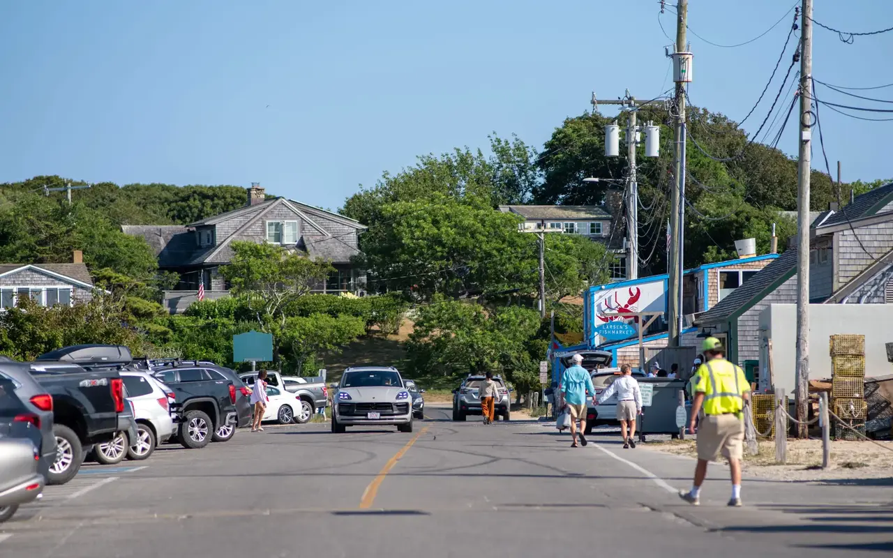People walking along the road toward the Menemsha fish markets on a summer afternoon with parked cars