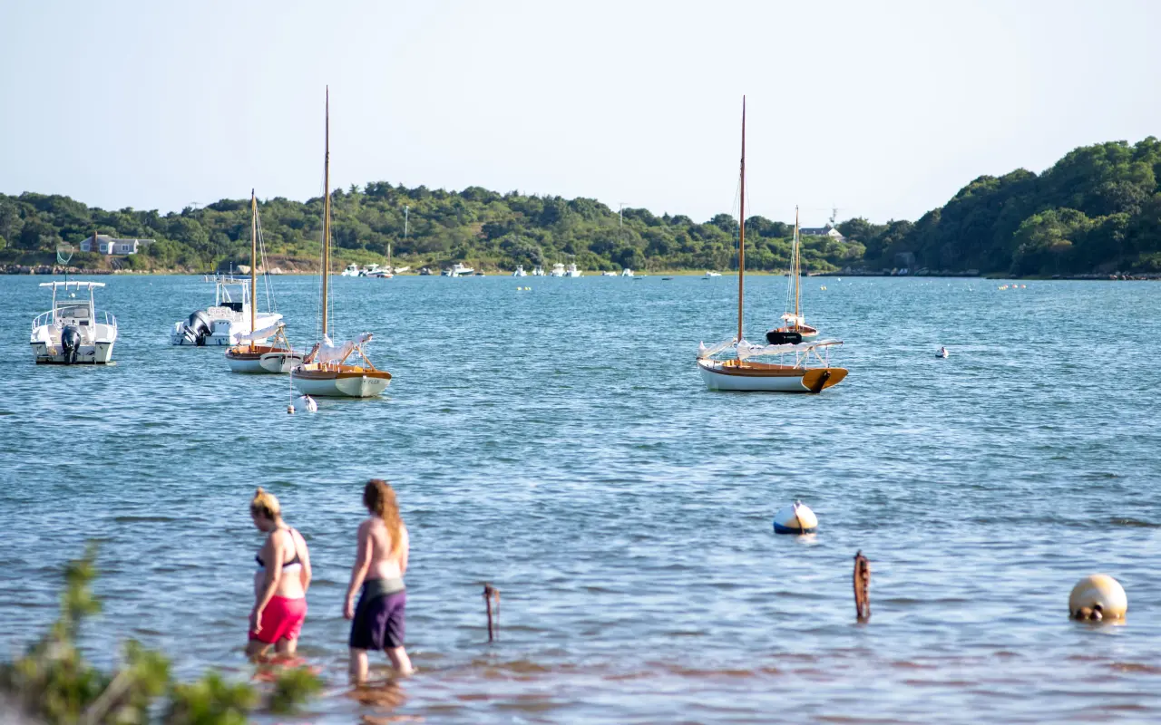 Children wading in calm water at Menemsha with sailboats moored behind them