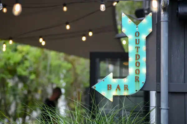 Outdoor bar arrow sign under string lights at Nomans