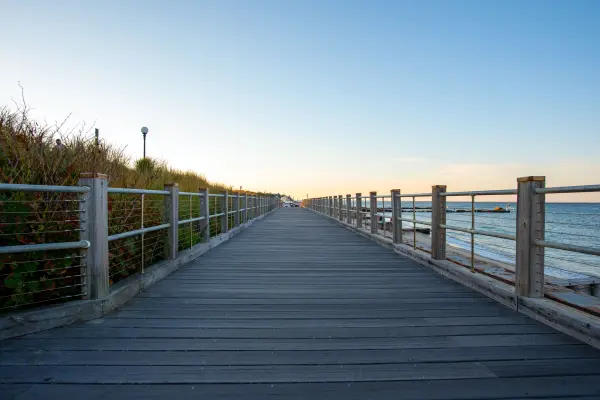 Empty beachside boardwalk stretching toward the harbor at dusk