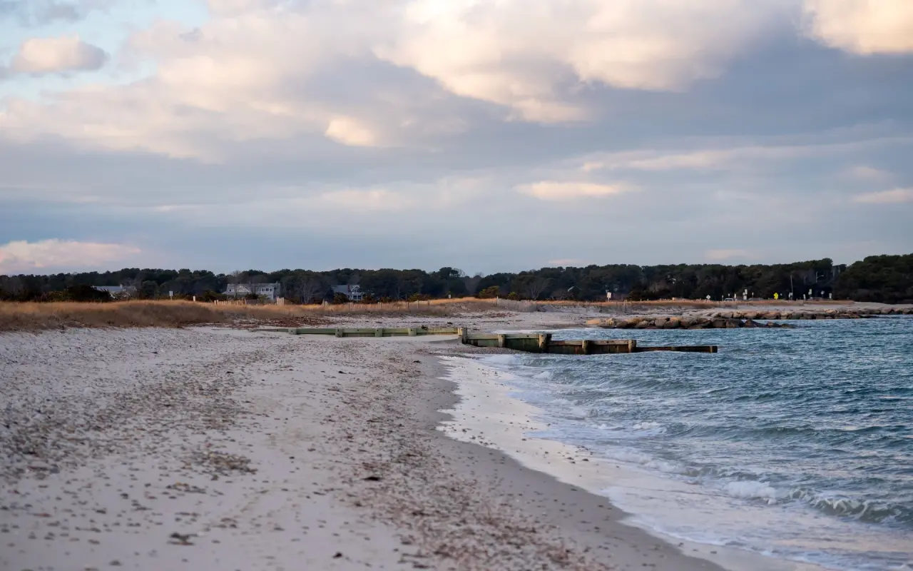 An empty State Beach in December with calm water, wooden and stone groins and dry beach grass under a cloudy sky