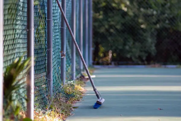 Push broom leaning on the fence of a pickleball court