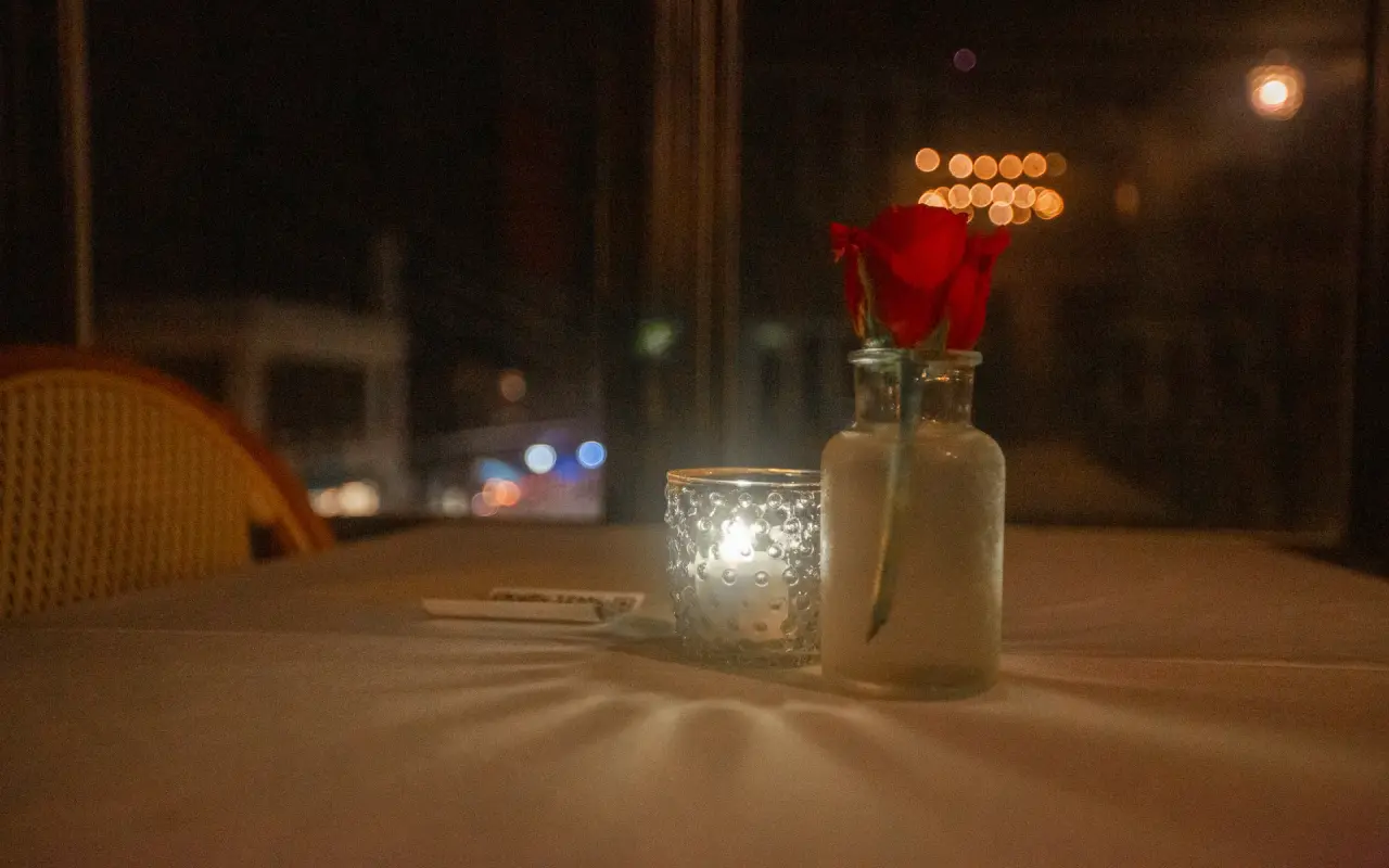 A candle and a single red rose on a restaurant table at night