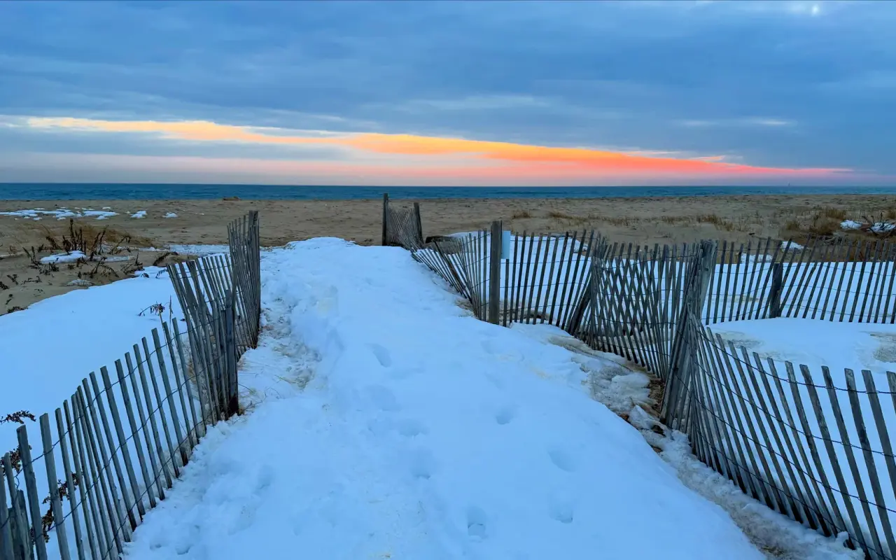 Snow-covered path between wooden sand fences leading to South Beach at dawn