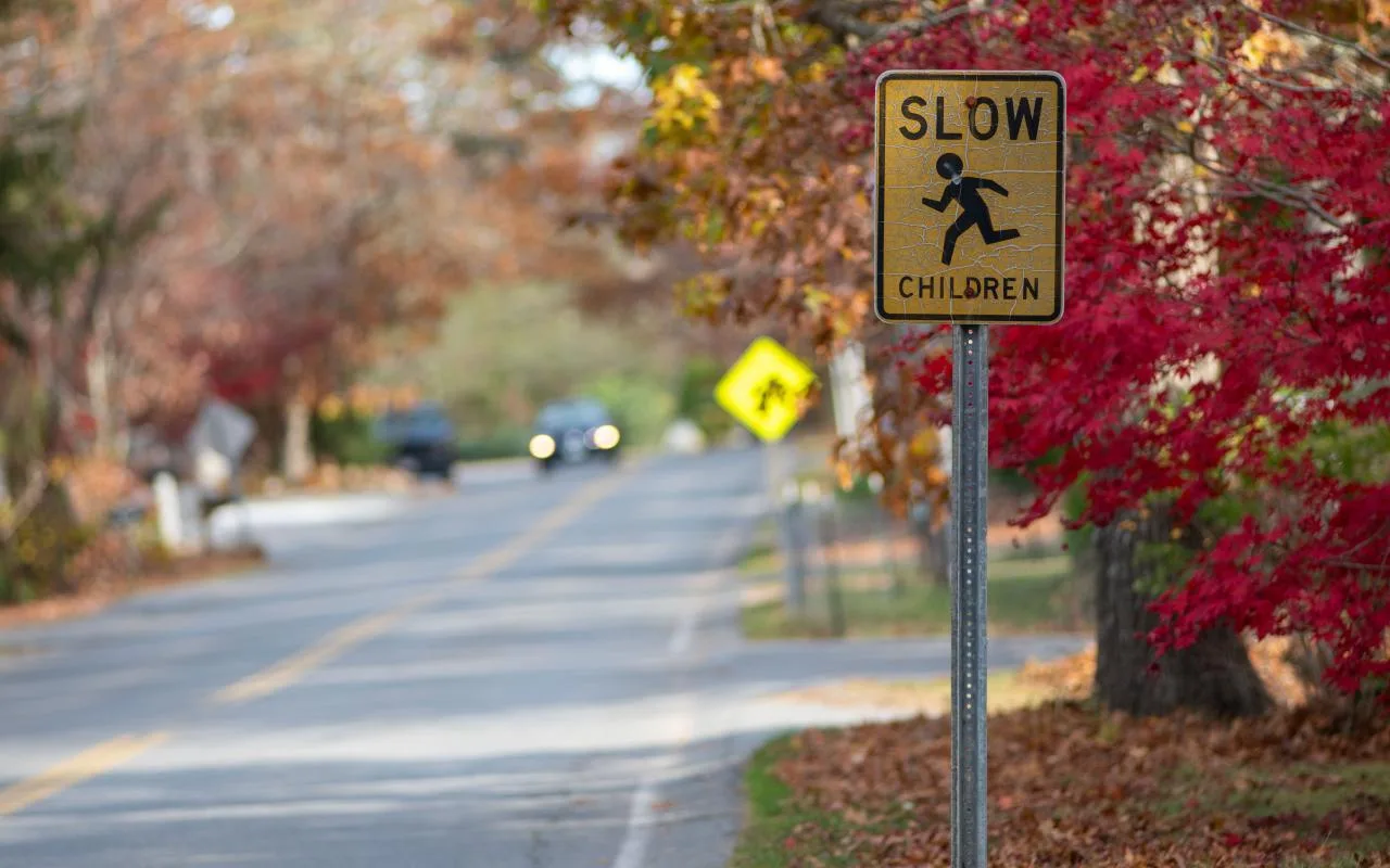 Yellow Slow Children road sign beside a two-lane road lined with red autumn maples