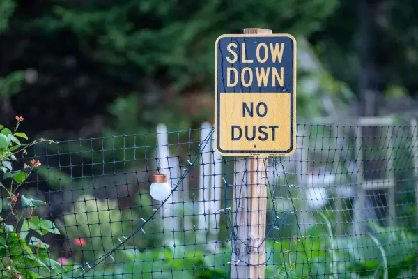Slow Down No Dust sign on a wooden post