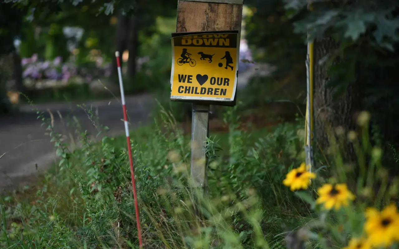 A yellow hand-painted sign reading slow down we love our children on a post beside a country road with black-eyed susans