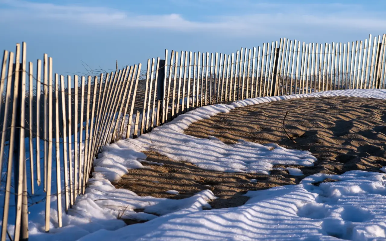 A sand fence casting shadows over a snow-dusted dune at South Beach