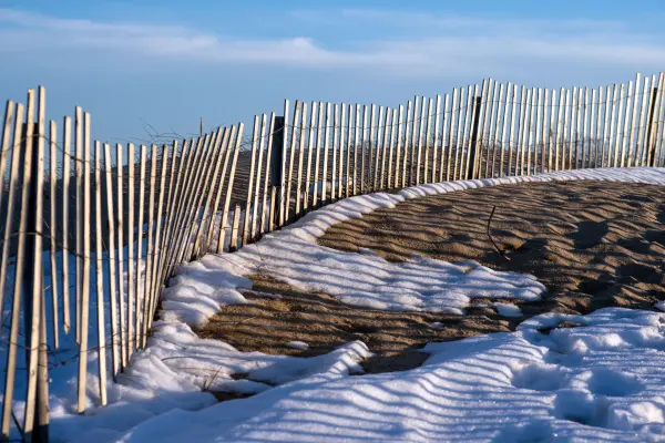 Sand fence casting shadows over snow-dusted dunes at South Beach