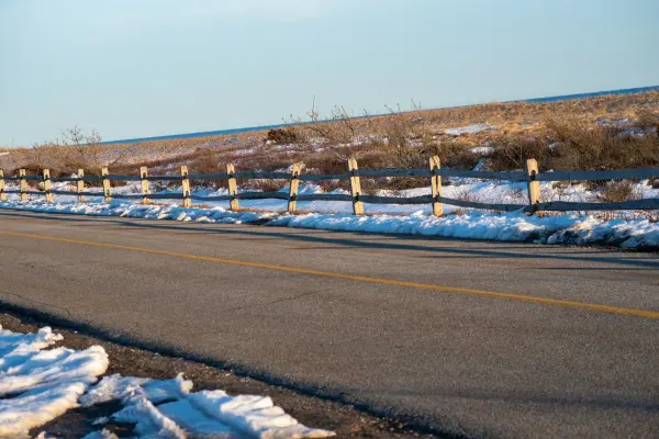 Melting snow along a split-rail fence by the shore