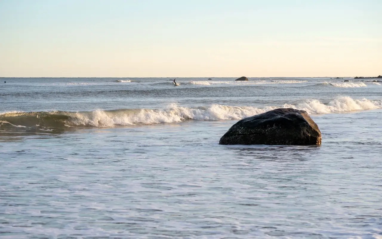 A lone surfer riding beyond a boulder in the shorebreak at Squibnocket