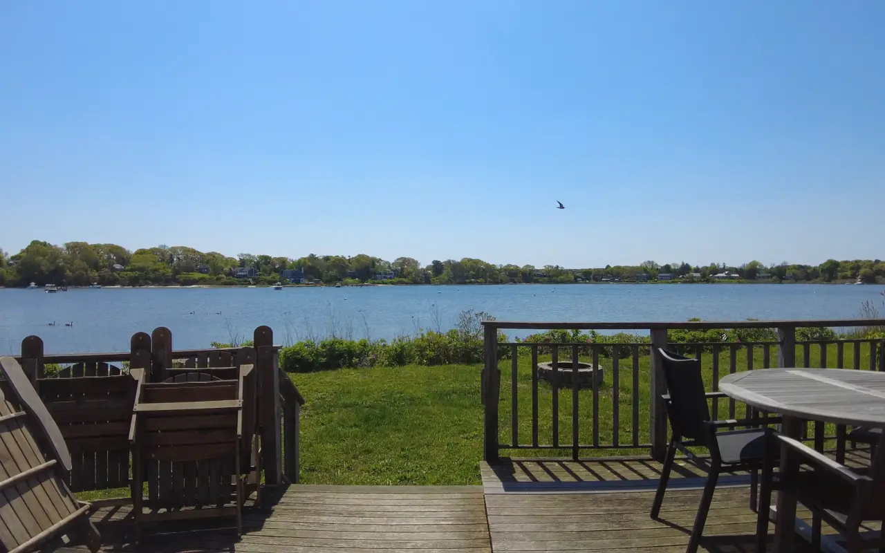 A wooden deck with a round table and chairs overlooking calm water and the far shore in Vineyard Haven