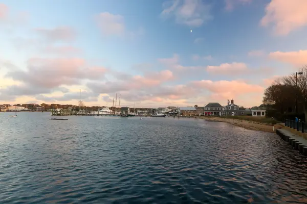 Pink cloud over the harbor at dusk, the masts and the shore lights coming on.