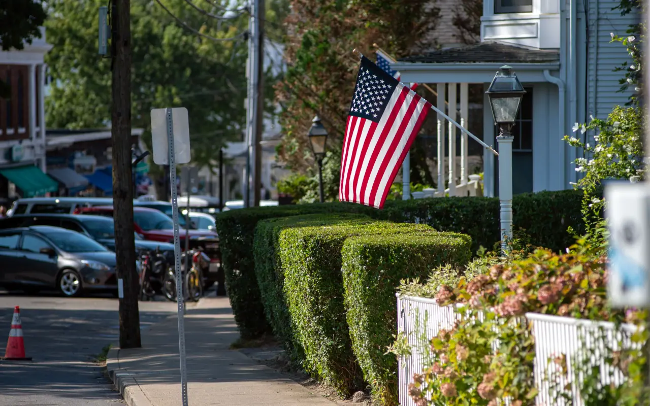 Trimmed hedges, a flag and parked cars along a street in Vineyard Haven