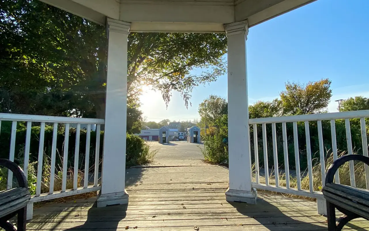 A covered wooden walkway with white railings at the Vineyard Haven ferry terminal, sun coming through the trees