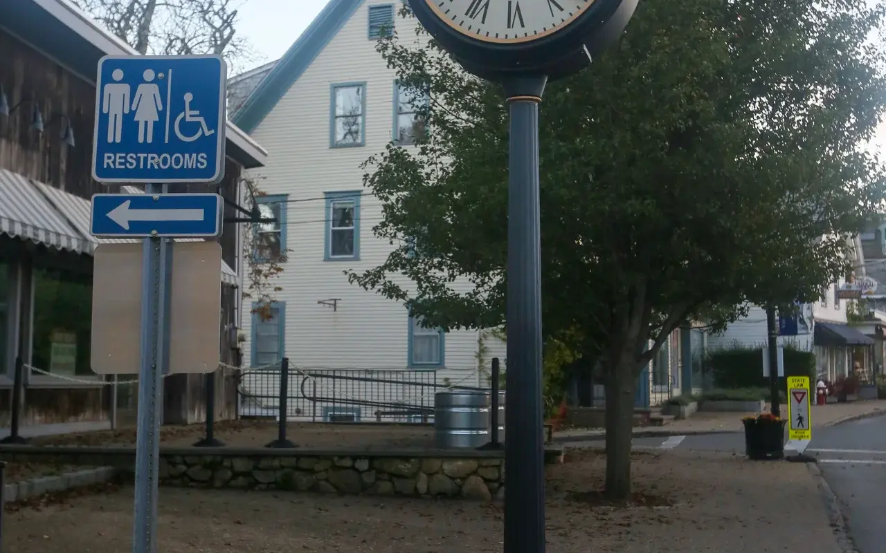 A post clock on a Main Street sidewalk in Vineyard Haven with a blue public restroom sign beneath it