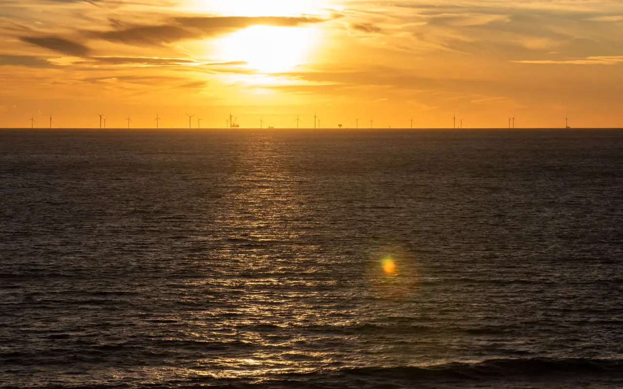 Sunset over the ocean with a row of offshore wind turbines visible on the horizon