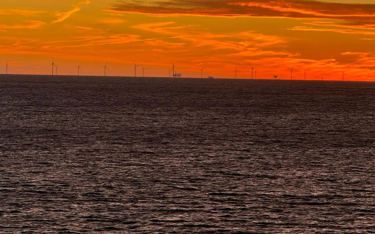 An orange sunset over a dark sea with small wind turbines visible on the far horizon