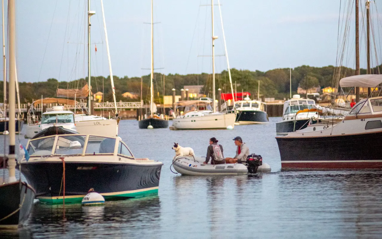 Motorboats and sailboats in Vineyard Haven harbor with a small tender and people aboard on a sunny day