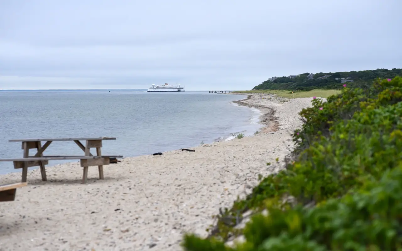 A picnic table on the sand at West Chop with a ferry passing on the water