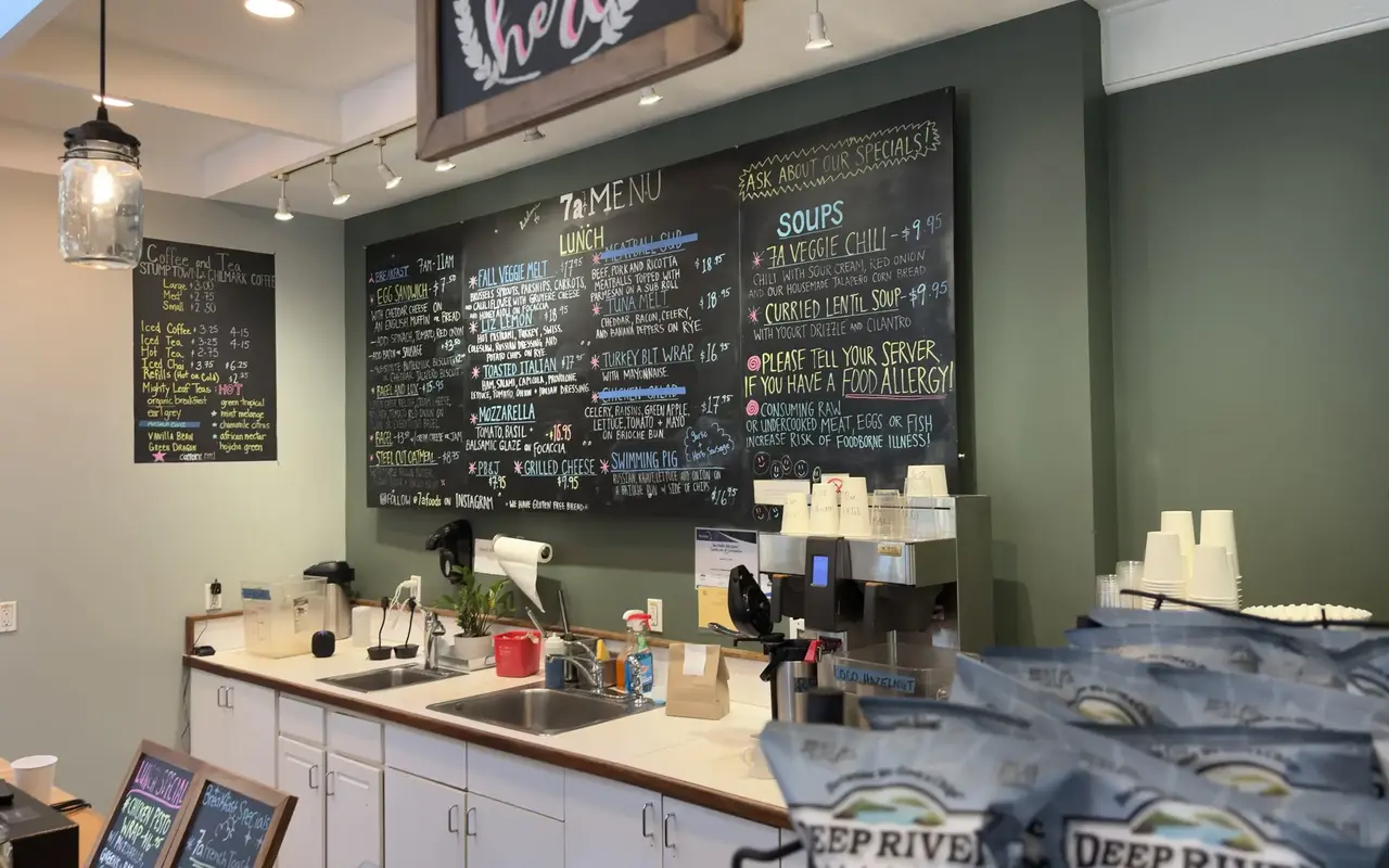 Chalkboard menu wall behind the counter at 7a Foods in West Tisbury, with lunch and soup boards, a coffee brewer and bags of chips