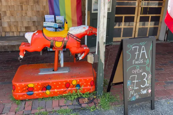 Chalkboard hours at 7a Foods, open 7 to 3 daily, with the coin-op horse standing guard