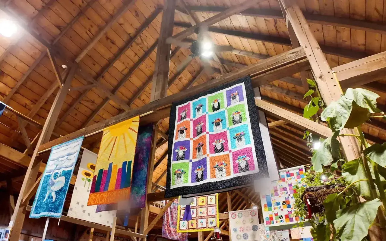 Quilts hanging from the wooden roof beams inside the Agricultural Hall in West Tisbury during the 2026 Agricultural Fair